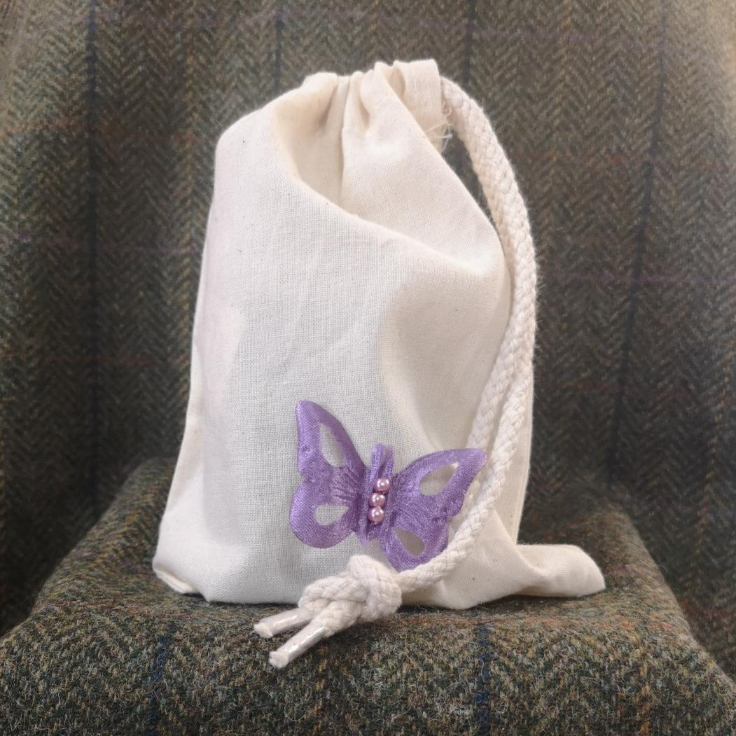 A Natural, cotton, drawstring bag with a complementary fabric butterfly accessory. It's able to hold your candle purchased from us.  